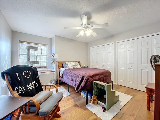 bedroom with ceiling fan, light hardwood / wood-style floors, a textured ceiling, and two closets