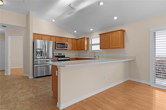 kitchen with sink, vaulted ceiling, light wood-type flooring, appliances with stainless steel finishes, and kitchen peninsula