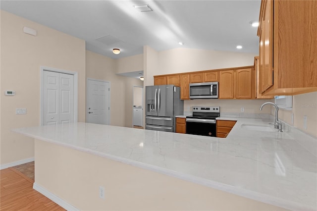 kitchen with vaulted ceiling, appliances with stainless steel finishes, sink, light stone counters, and kitchen peninsula