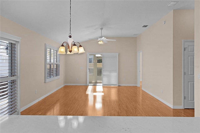 unfurnished dining area with ceiling fan with notable chandelier, vaulted ceiling, and light hardwood / wood-style floors