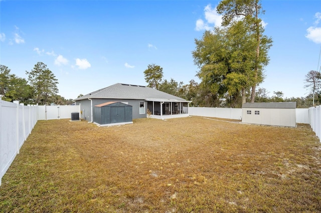 rear view of property featuring a sunroom, a lawn, central air condition unit, and a storage shed