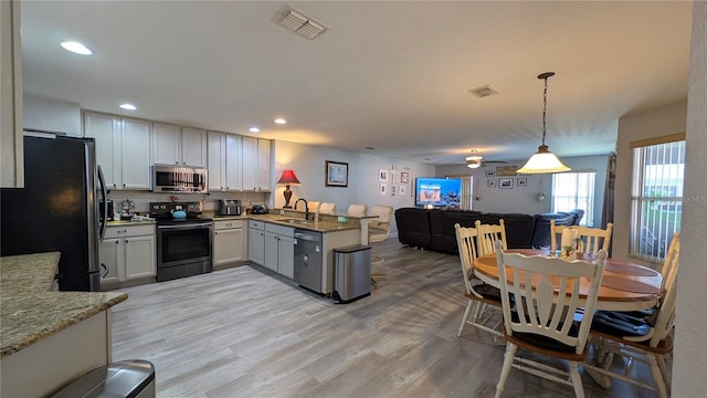 kitchen featuring decorative light fixtures, light wood-type flooring, appliances with stainless steel finishes, kitchen peninsula, and light stone countertops