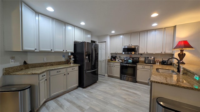 kitchen with stone counters, appliances with stainless steel finishes, sink, and light hardwood / wood-style flooring