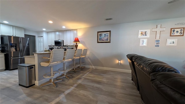 kitchen with white cabinetry, a breakfast bar area, stainless steel appliances, and wood-type flooring