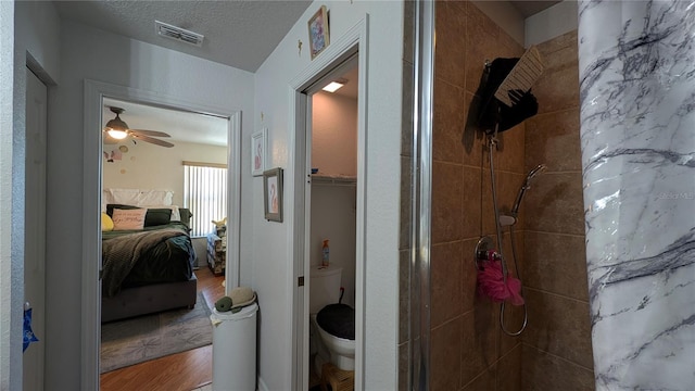 bathroom with toilet, a textured ceiling, a tile shower, hardwood / wood-style flooring, and ceiling fan