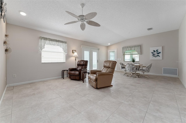 living area with lofted ceiling, ceiling fan, a textured ceiling, and light tile patterned flooring