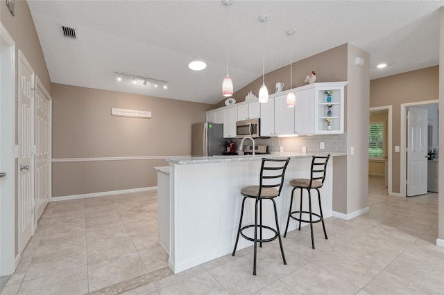 kitchen with appliances with stainless steel finishes, decorative light fixtures, white cabinetry, a kitchen bar, and kitchen peninsula