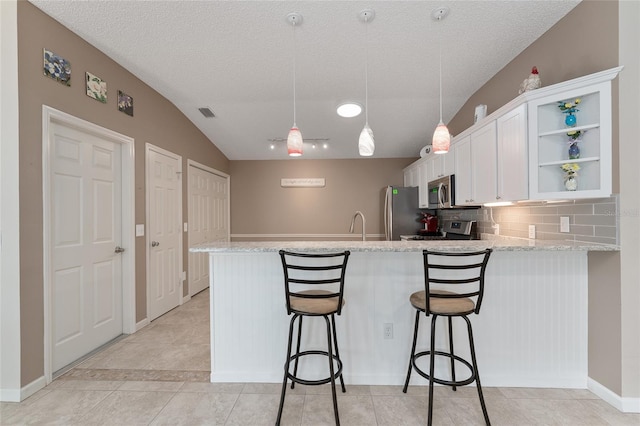 kitchen featuring appliances with stainless steel finishes, white cabinetry, tasteful backsplash, a kitchen bar, and kitchen peninsula