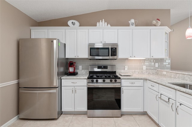 kitchen with appliances with stainless steel finishes, vaulted ceiling, decorative backsplash, and white cabinets