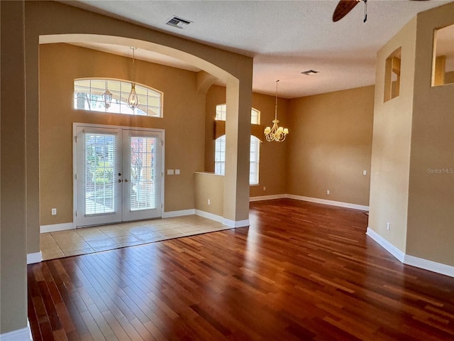 foyer with ceiling fan with notable chandelier, wood-type flooring, french doors, and a textured ceiling