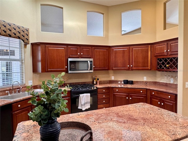 kitchen featuring black gas range, sink, light stone countertops, and a high ceiling