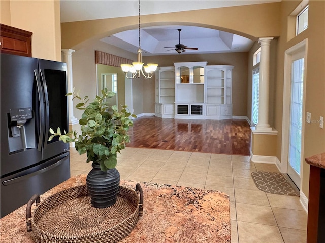 kitchen with a raised ceiling, light tile patterned flooring, decorative columns, and black fridge with ice dispenser