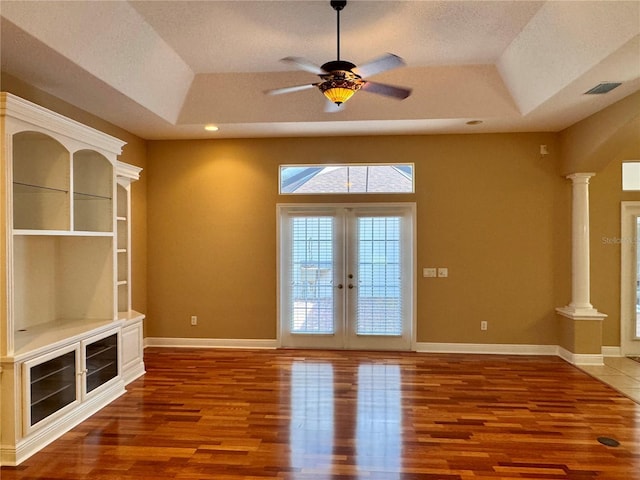 unfurnished living room featuring built in shelves, a raised ceiling, hardwood / wood-style floors, and ornate columns