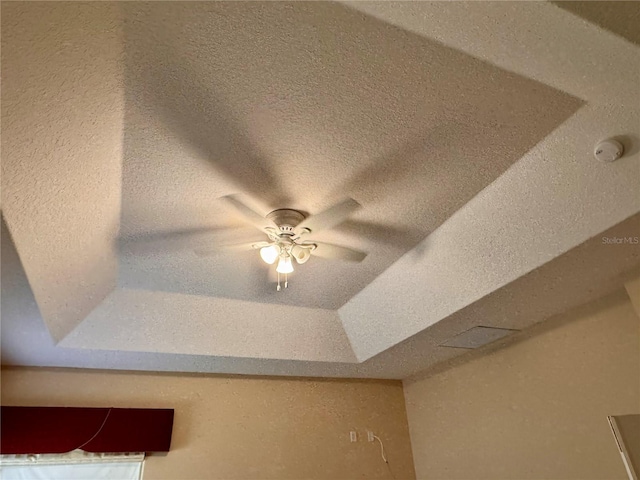 interior details featuring ceiling fan and a tray ceiling