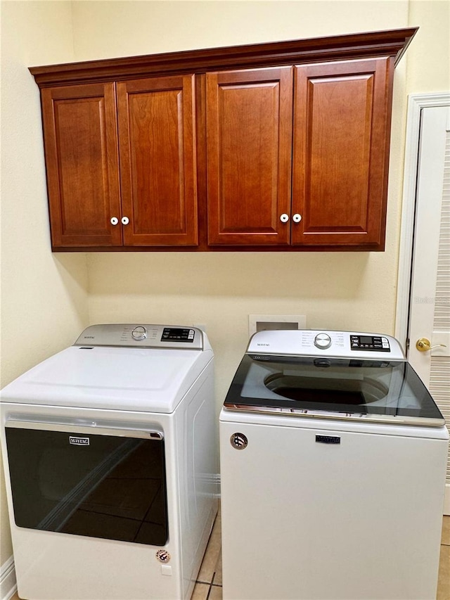 clothes washing area with light tile patterned floors, cabinets, and washing machine and clothes dryer