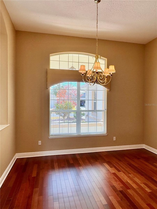 empty room with a textured ceiling, a notable chandelier, and dark hardwood / wood-style flooring