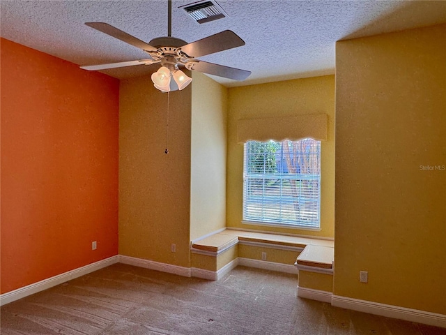 empty room with ceiling fan, light colored carpet, and a textured ceiling