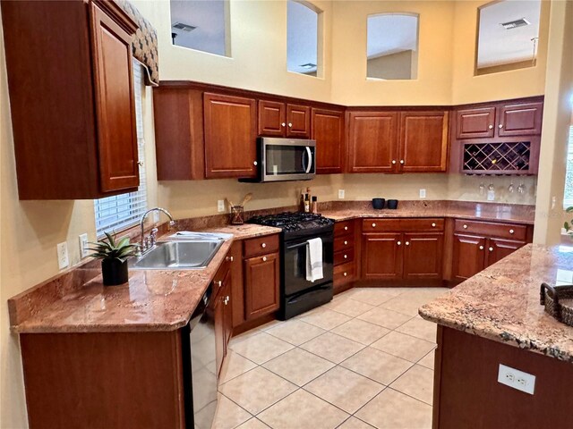 kitchen with light stone countertops, a sink, black appliances, visible vents, and a towering ceiling
