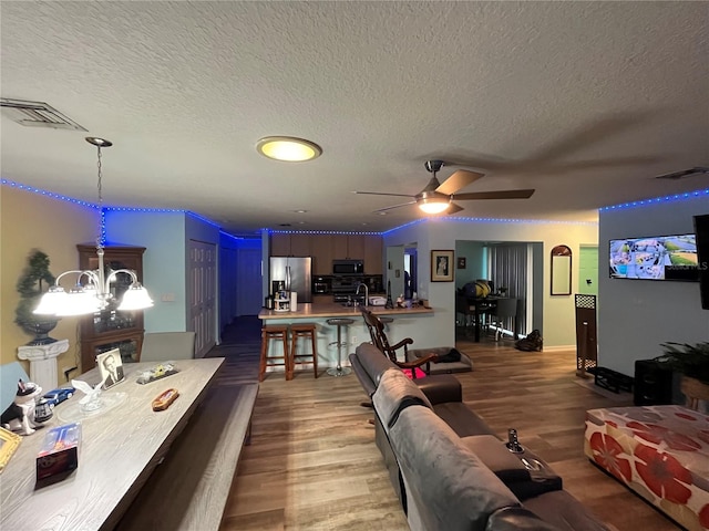 living room featuring hardwood / wood-style flooring, ceiling fan with notable chandelier, and a textured ceiling