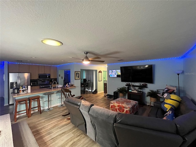 living room with sink, ceiling fan, a textured ceiling, and light wood-type flooring