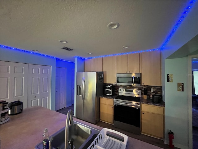 kitchen with light brown cabinetry, sink, stainless steel appliances, and a textured ceiling