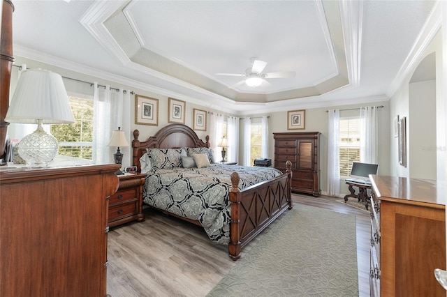 bedroom featuring crown molding, ceiling fan, a tray ceiling, and light hardwood / wood-style flooring