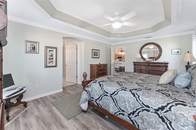 bedroom with crown molding, a tray ceiling, ceiling fan, and light wood-type flooring