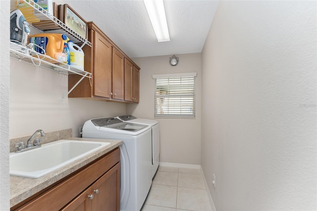 washroom featuring washing machine and clothes dryer, sink, cabinets, a textured ceiling, and light tile patterned floors