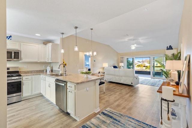 kitchen with sink, decorative light fixtures, vaulted ceiling, stainless steel appliances, and white cabinets