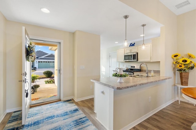 kitchen featuring sink, hanging light fixtures, stainless steel appliances, light hardwood / wood-style floors, and kitchen peninsula