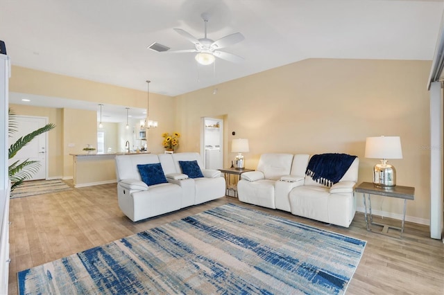 living room featuring vaulted ceiling, ceiling fan with notable chandelier, and light hardwood / wood-style floors