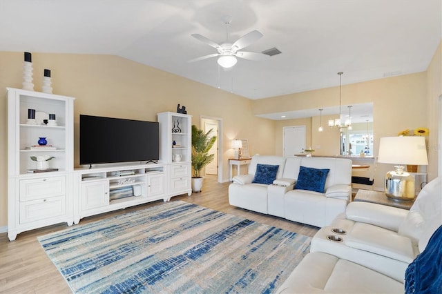 living room featuring ceiling fan with notable chandelier, light hardwood / wood-style flooring, and vaulted ceiling