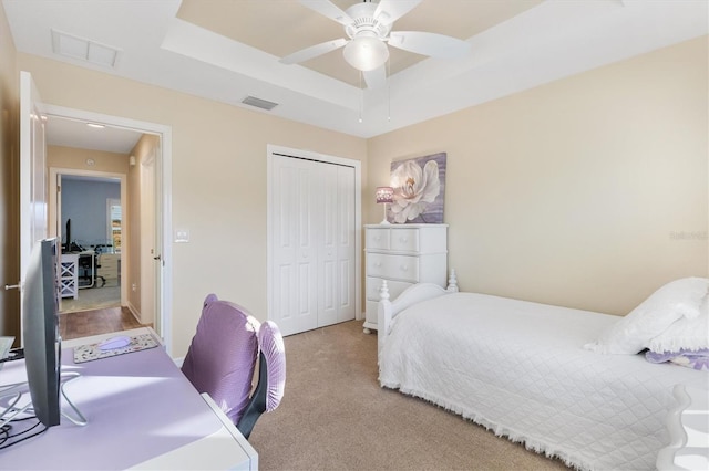 bedroom featuring ceiling fan, a tray ceiling, light carpet, and a closet