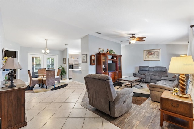 tiled living room with ceiling fan with notable chandelier