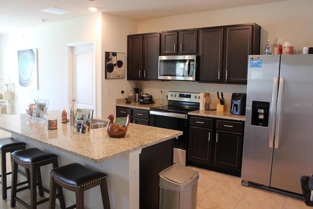 kitchen featuring a kitchen island, appliances with stainless steel finishes, a breakfast bar, light tile patterned floors, and light stone countertops