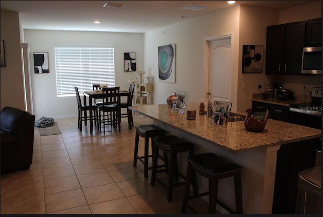 kitchen featuring light tile patterned floors, sink, a breakfast bar, appliances with stainless steel finishes, and an island with sink