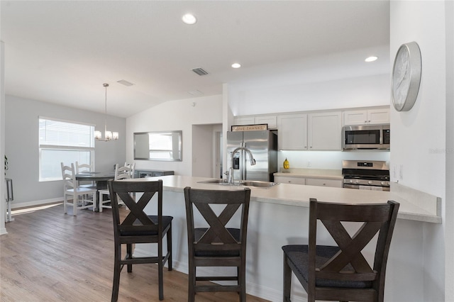 kitchen with a kitchen bar, sink, white cabinetry, decorative light fixtures, and stainless steel appliances