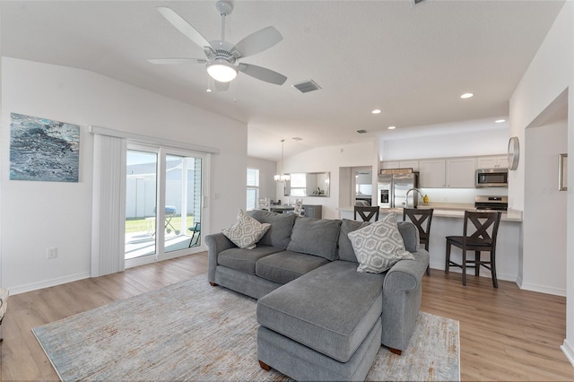 living room with vaulted ceiling, ceiling fan with notable chandelier, and light wood-type flooring