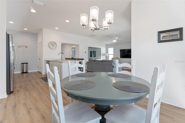 dining room featuring vaulted ceiling, sink, ceiling fan with notable chandelier, and light hardwood / wood-style flooring