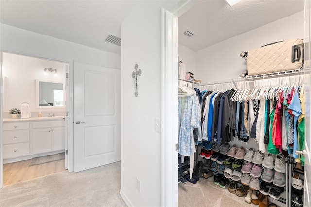 walk in closet with sink and light colored carpet