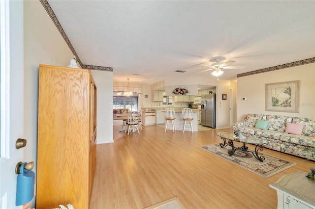 living room with ceiling fan, a textured ceiling, and light hardwood / wood-style flooring