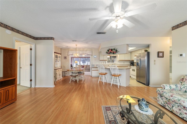 living room featuring ceiling fan, a textured ceiling, and light wood-type flooring