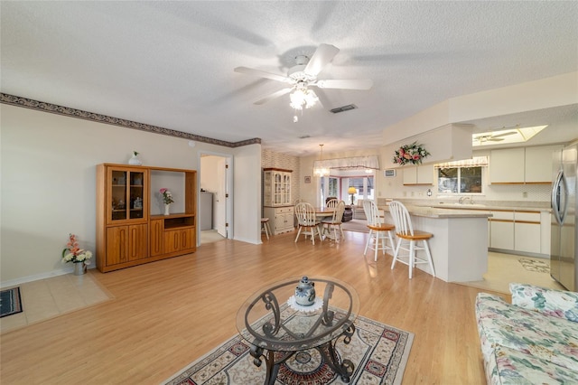 living room featuring ceiling fan, sink, light hardwood / wood-style floors, and a textured ceiling