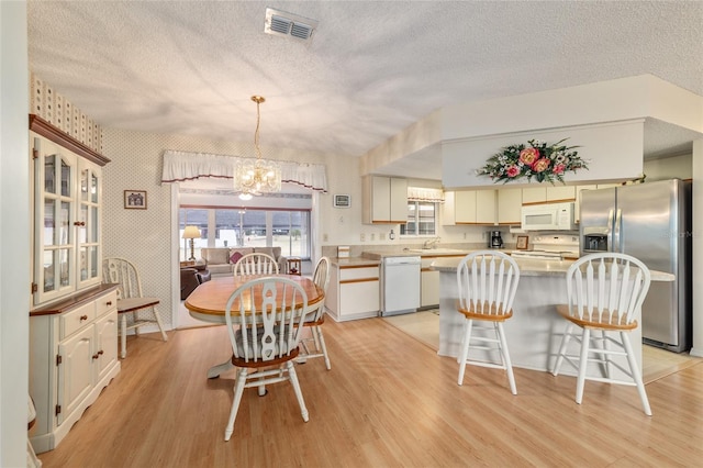 dining space with light hardwood / wood-style floors, sink, a textured ceiling, and a notable chandelier