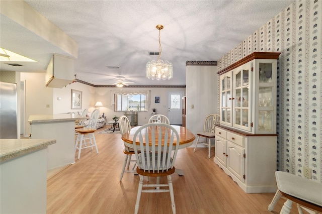 dining room with ornamental molding, ceiling fan with notable chandelier, a textured ceiling, and light wood-type flooring