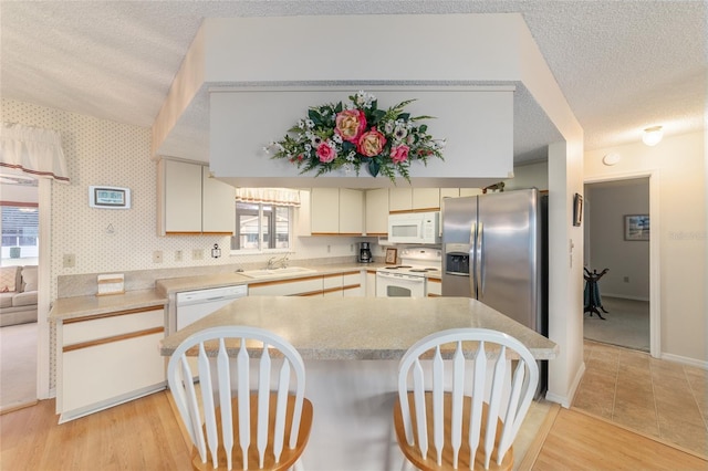 kitchen with sink, white appliances, kitchen peninsula, a healthy amount of sunlight, and light wood-type flooring