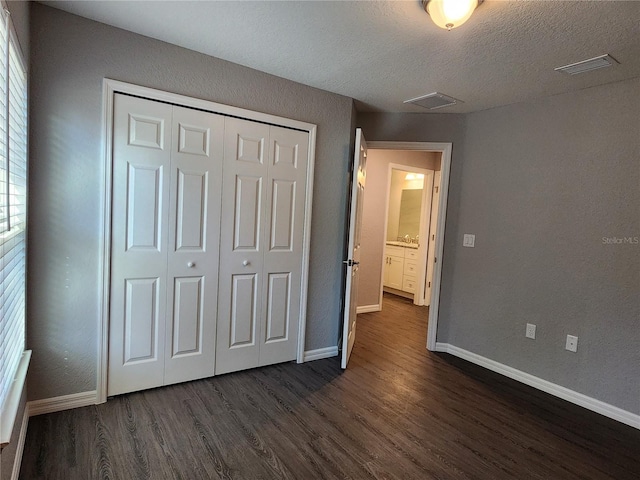 unfurnished bedroom featuring a textured ceiling, dark hardwood / wood-style flooring, and a closet