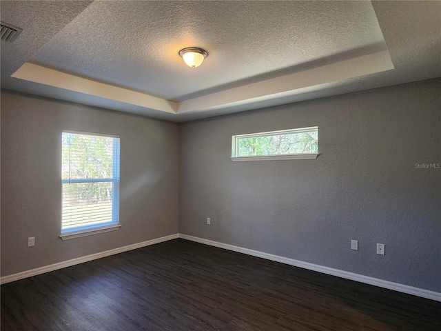 empty room with dark wood-type flooring, a raised ceiling, and a textured ceiling