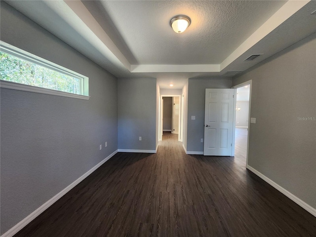 empty room with a tray ceiling, dark hardwood / wood-style floors, and a textured ceiling