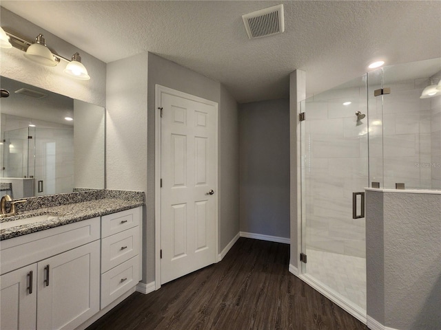 bathroom with hardwood / wood-style flooring, vanity, a shower with door, and a textured ceiling